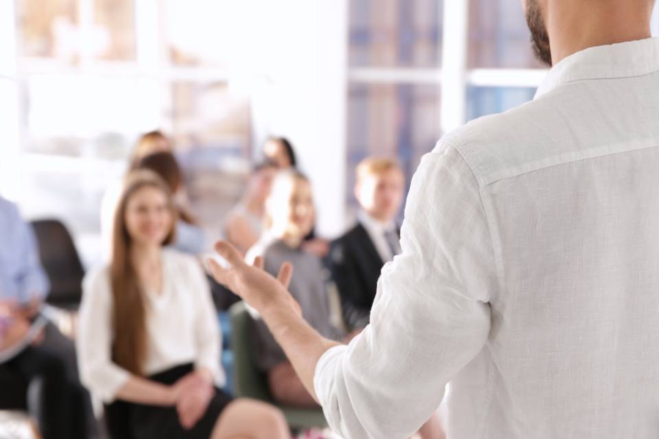 Persona con camisa blanca dando una charla a un grupo de ejecutivos